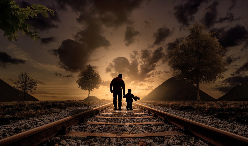 silhouette of father and son walking down train tracks.